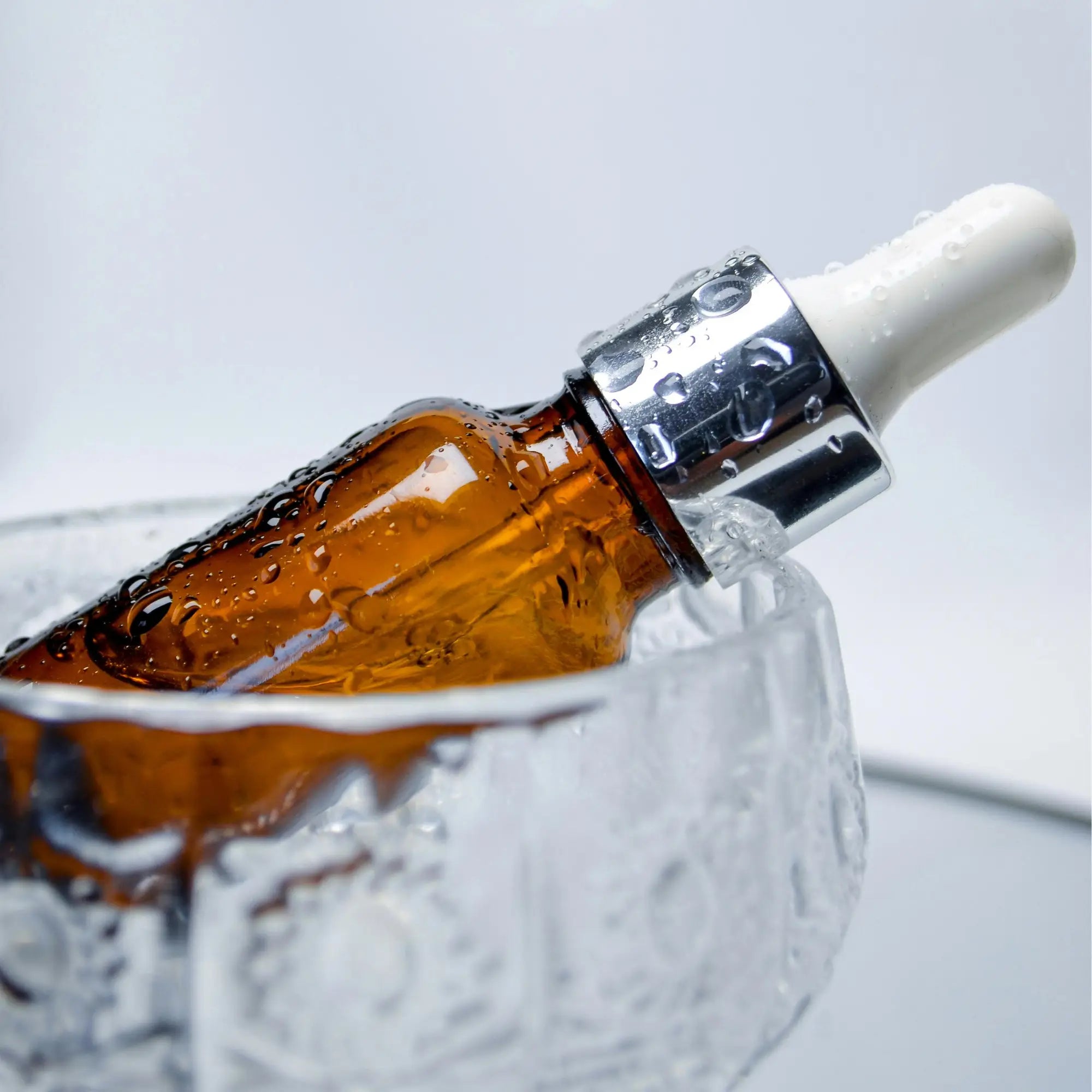 Brown glass dropper bottle with a white cap in a glass bowl on a light gray background